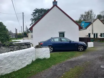 a blue car parked in front of a white house at The WEE HOUSE Balvicar Isle of Seil in Balvicar