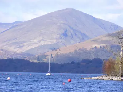 a sailboat in the water with a mountain in the background at Dingieshowe Cottage in Lennoxtown
