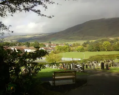 a bench in a cemetery with mountains in the background at Dingieshowe Cottage in Lennoxtown