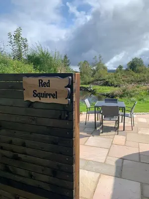 a sign that reads red squirrel with a table and chairs at Red Squirrel Pod with Hot Tub in Oban