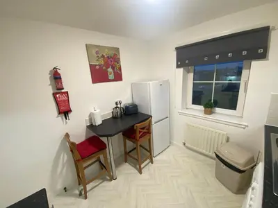 a small kitchen with a table and a refrigerator at Prime Duloch Bridge View by TBA in Dunfermline