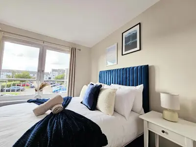 a bedroom with a bed with a blue headboard and a window at Modern 5 Bedroom Townhouse with Free Parking in Glasgow