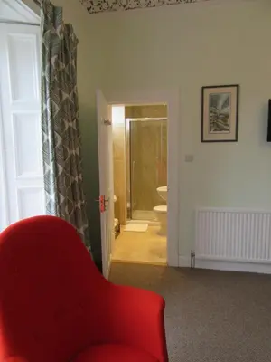 a red chair in a living room with a bathroom at Middleton House Bed and Breakfast in Auchterarder