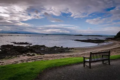 a bench sitting next to a body of water at Seaside Place, Aberdour in Aberdour