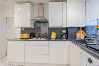 a white kitchen with white cabinets and appliances at Henry Bell - Cosy 2-bedroom cottage in Helensburgh
