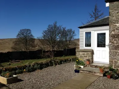 a cottage with a white door and a garden at Langside in Stirling