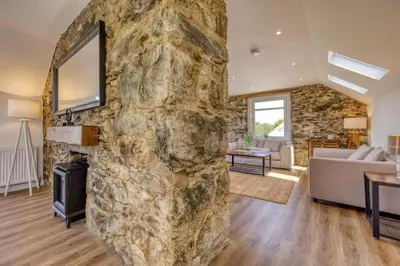 a large stone wall in a living room with a fireplace at Blar Cottage (Private Sauna + Fast Starlink Wifi) in Hayfield