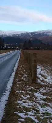 a road with snow on the ground next to a fence at Aquila Retreats in Comrie