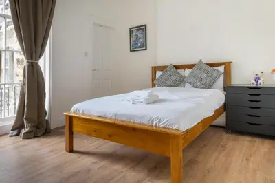 a bedroom with a bed with white sheets and a window at Bright High-Ceiling 2BD Flat - Central Edinburgh! in Edinburgh