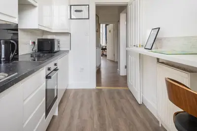 a kitchen with white cabinets and a wooden floor at Bright High-Ceiling 2BD Flat - Central Edinburgh! in Edinburgh