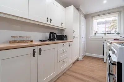 a kitchen with white cabinets and a window at Shaw Apartment in Glasgow