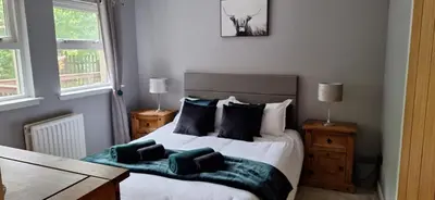 a bedroom with a bed with two tables and two windows at Ben Vorlich Cottage in Tarbet