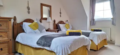 a bedroom with two beds with white and yellow pillows at Ben Vorlich Cottage in Tarbet