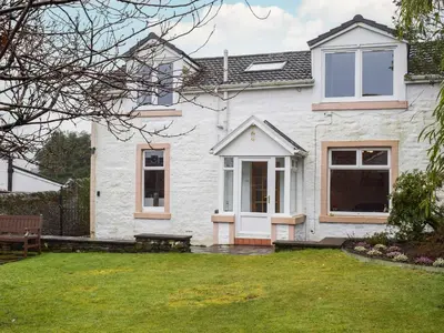 a white house with a bench in the yard at Wayside Cottage in Dunoon