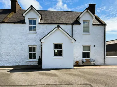 a white house with a bench in front of it at The Old Cheese Loft in Colfin