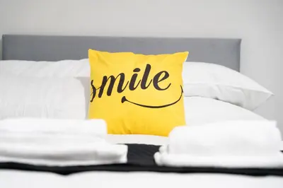 a yellow pillow with a smile written on it on a bed at Bell Apartment in Airdrie