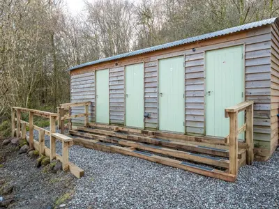 a wooden cabin with three doors and a bench at Cobleland Campsite in Gartmore