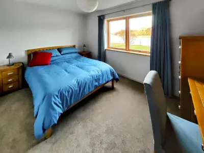 a bedroom with a bed with a blue comforter and a window at Tulamain in Ardfern