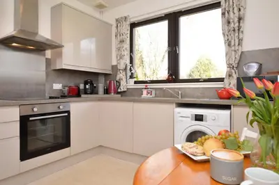 a kitchen with white cabinets and a table with a plate of food at Heronlea Cottage in Dunoon
