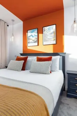 a bedroom with a large bed with an orange wall at The Stylish 3-Bedroom Maisonette Retreat in Stirling