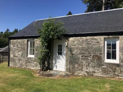 an old stone house with a white door and a tree at Ellary Cottage in Stonefield