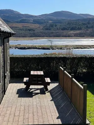 a wooden deck with a picnic table next to a river at The Lodge in Lochgilphead