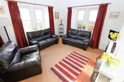 a living room with black leather furniture and windows at The Lodge in Lochgilphead