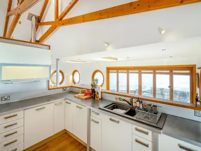 a kitchen with white cabinets and a sink and windows at Shore House in Kilcreggan