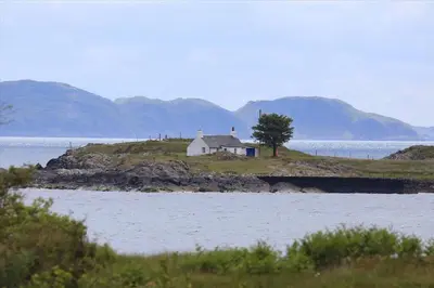 a small white house on an island in the water at Archie's Cottage in Auchnacraig