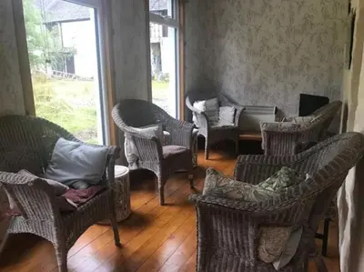 a room with wicker chairs and tables and windows at Barrachandroman Farmhouse in Lochbuie