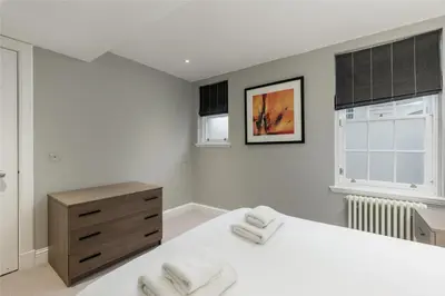 a bedroom with a white bed and a dresser and windows at Destiny Scotland - Hill Street Apartments in Edinburgh