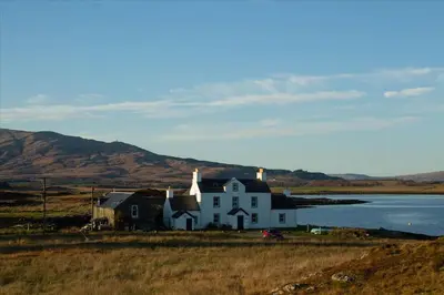 a white house on the shore of a body of water at Old Ferry House in Auchnacraig