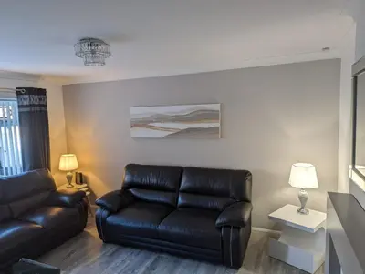 a living room with a leather couch and a table at Lovely 2 Bedroom Terrace House in Coatbridge