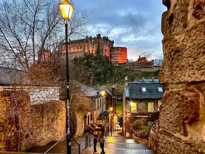 a couple of people walking down a street with a castle at E'holidays in Edinburgh