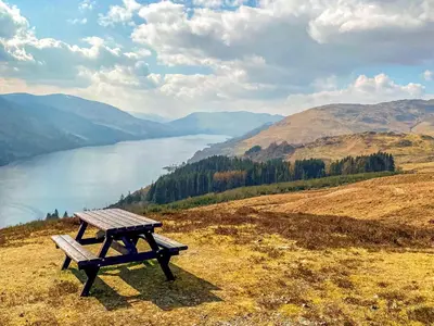 a picnic table on top of a hill overlooking a lake at Craigdarroch Cottage in Saint Fillans
