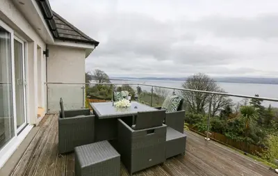 a patio with a table and chairs on a balcony at Viewpoint Villa - Luxury 4 Bedroom villa with elevated views in Rothesay