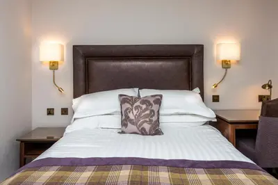 a large bed with a brown headboard and two lamps at Macdonald Inchyra Hotel & Spa in Falkirk