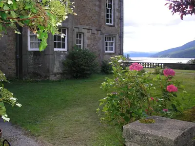 an old brick building with pink flowers in the yard at Butlers Quarters Apartment in Cairndow