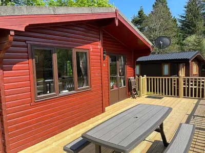 a red cabin with a picnic table on a deck at Loch Lomond Lodge in Rowardennan