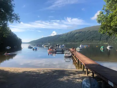 a dock with boats on a lake next to a mountain at Loch Lomond Lodge in Rowardennan