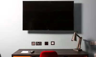 a flat screen tv on a wall with a red chair at Village Hotel Edinburgh in Edinburgh