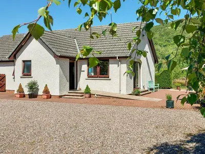 a white house with a bench in front of it at Roe Deer Cottage in North Ballachulish