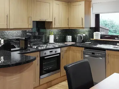 a kitchen with wooden cabinets and black counter tops at Roe Deer Cottage in North Ballachulish