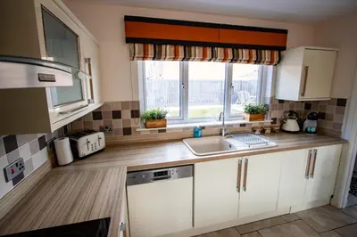 a kitchen with white cabinets and a sink and a window at Harvest House with Games Room in Stirling