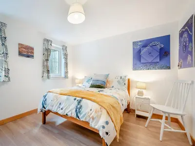 a bedroom with a bed and a white chair at Postbox Cottage in Lochranza