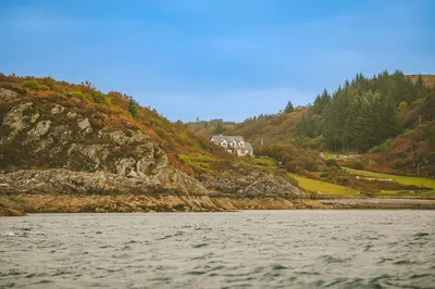 a house on a hill next to a body of water at Seal Bay Cottage in Kilfinan