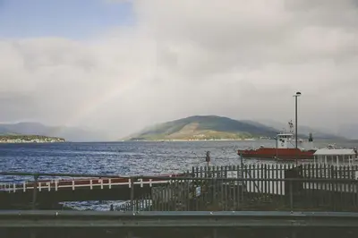a boat on the water with a rainbow in the sky at Seal Bay Cottage in Kilfinan