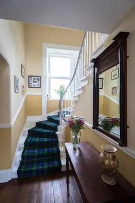a hallway with stairs with a vase of flowers on a table at Kilmaronock Manse B&B in Drymen