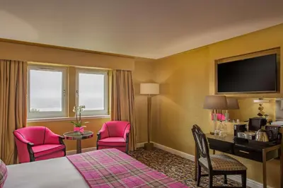 a hotel room with a bed and a desk and chairs at Gleddoch Golf & Spa Resort in Langbank