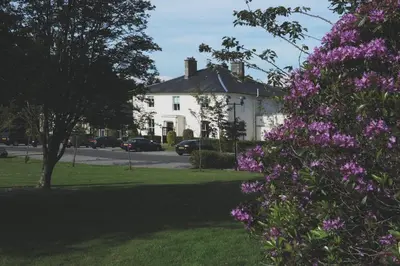 a white house with purple flowers in a yard at Macdonald Crutherland House in East Kilbride